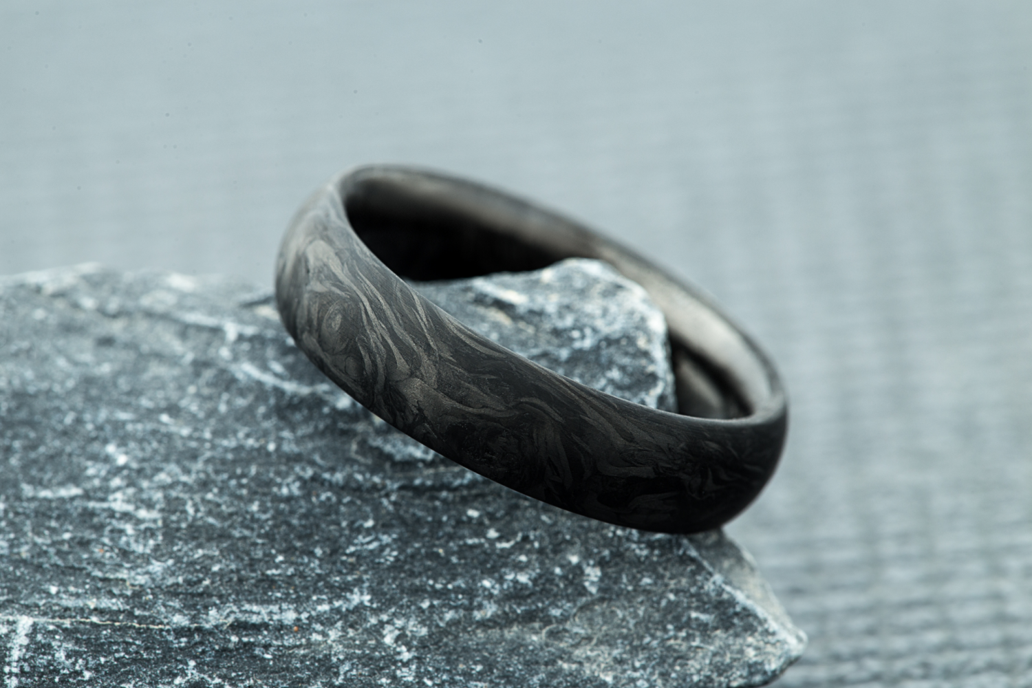 Forged carbon fiber radius ring displayed on a rock. 