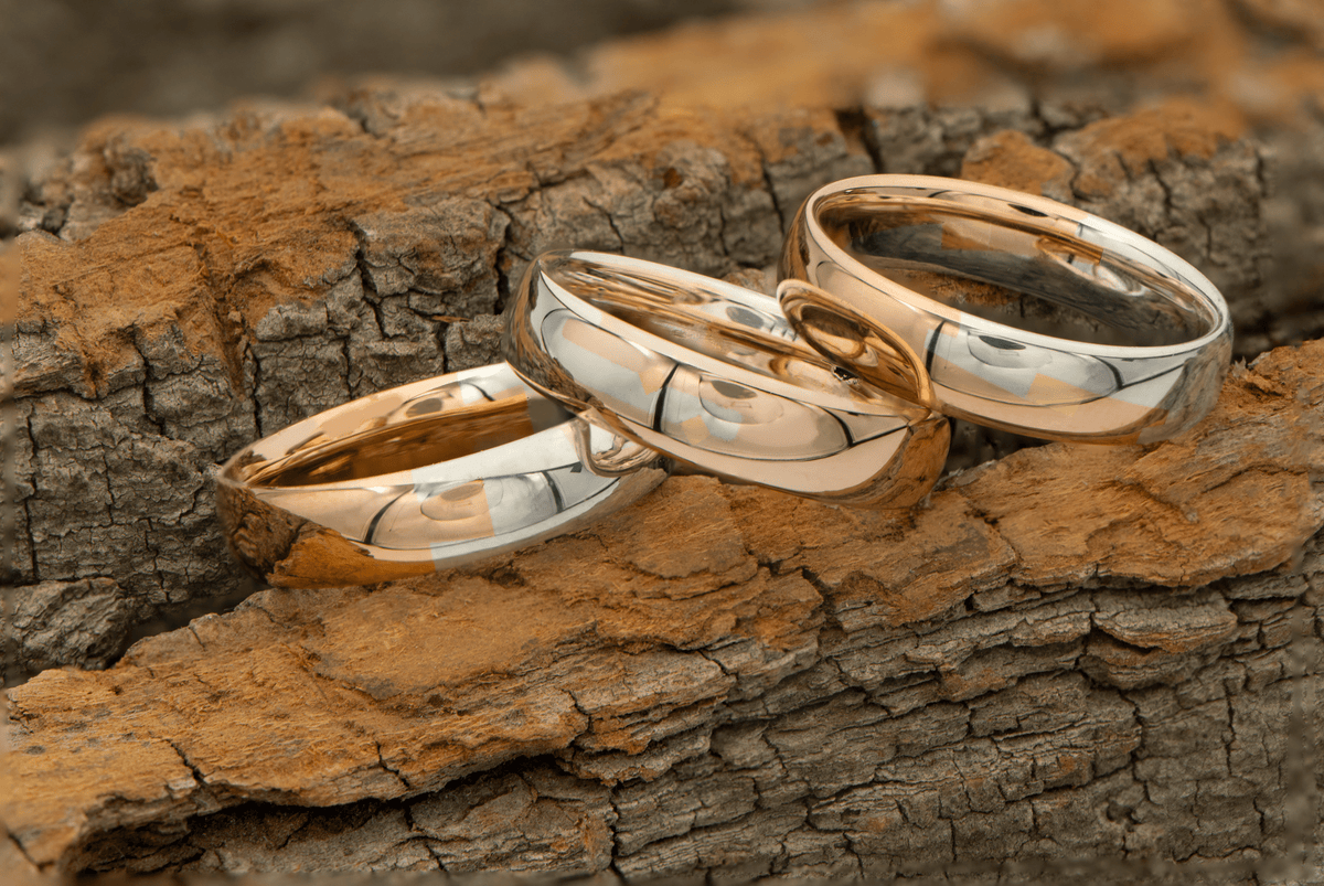 Three silver and gold joinery rings displayed on driftwood.