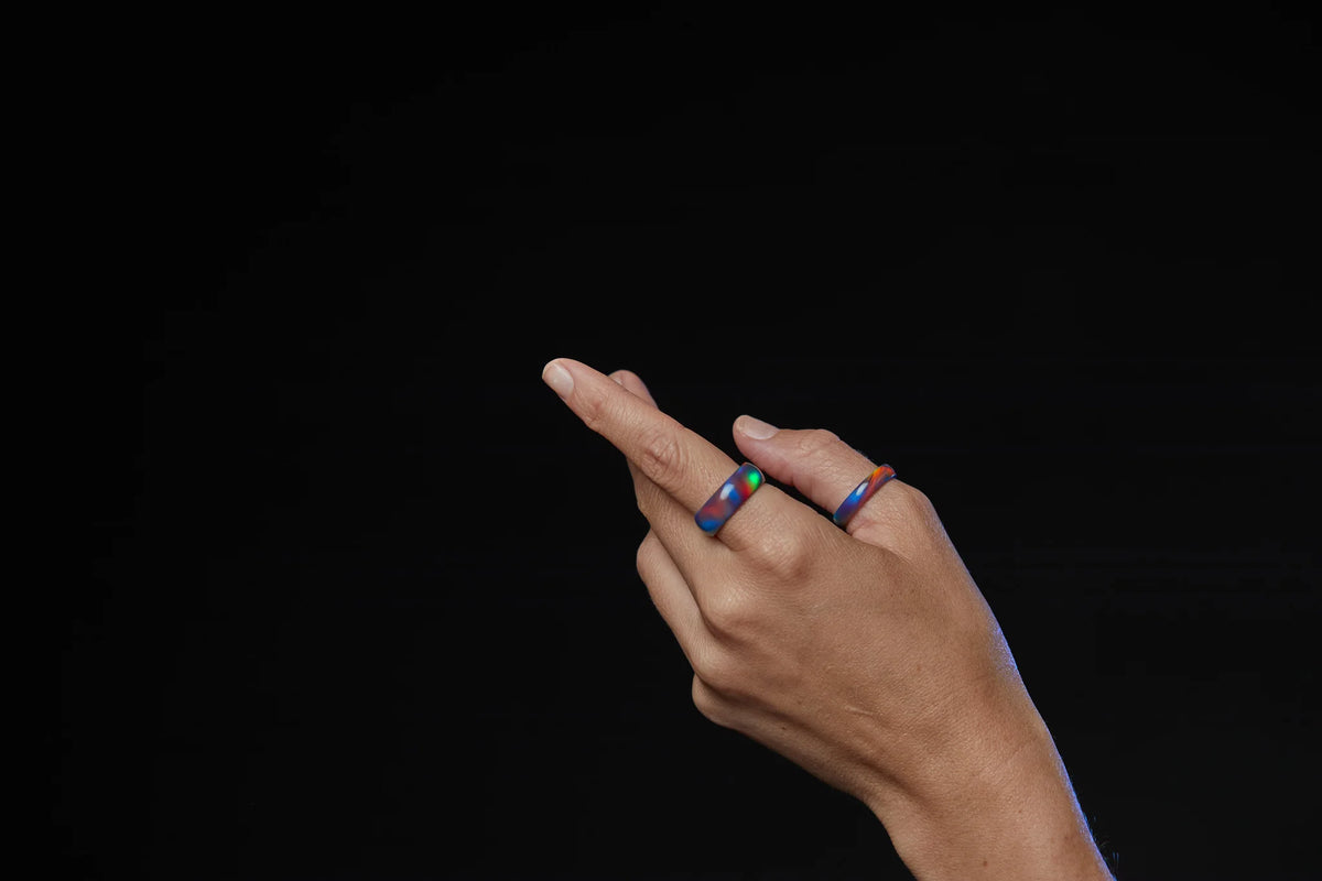 One 4mm multi-colored opal ring and one 8mm multi-colored opal ring featured on a hand model. 