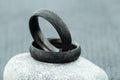 Two carbon fiber rings with satin finish balancing on top of one another, placed on a rock. 