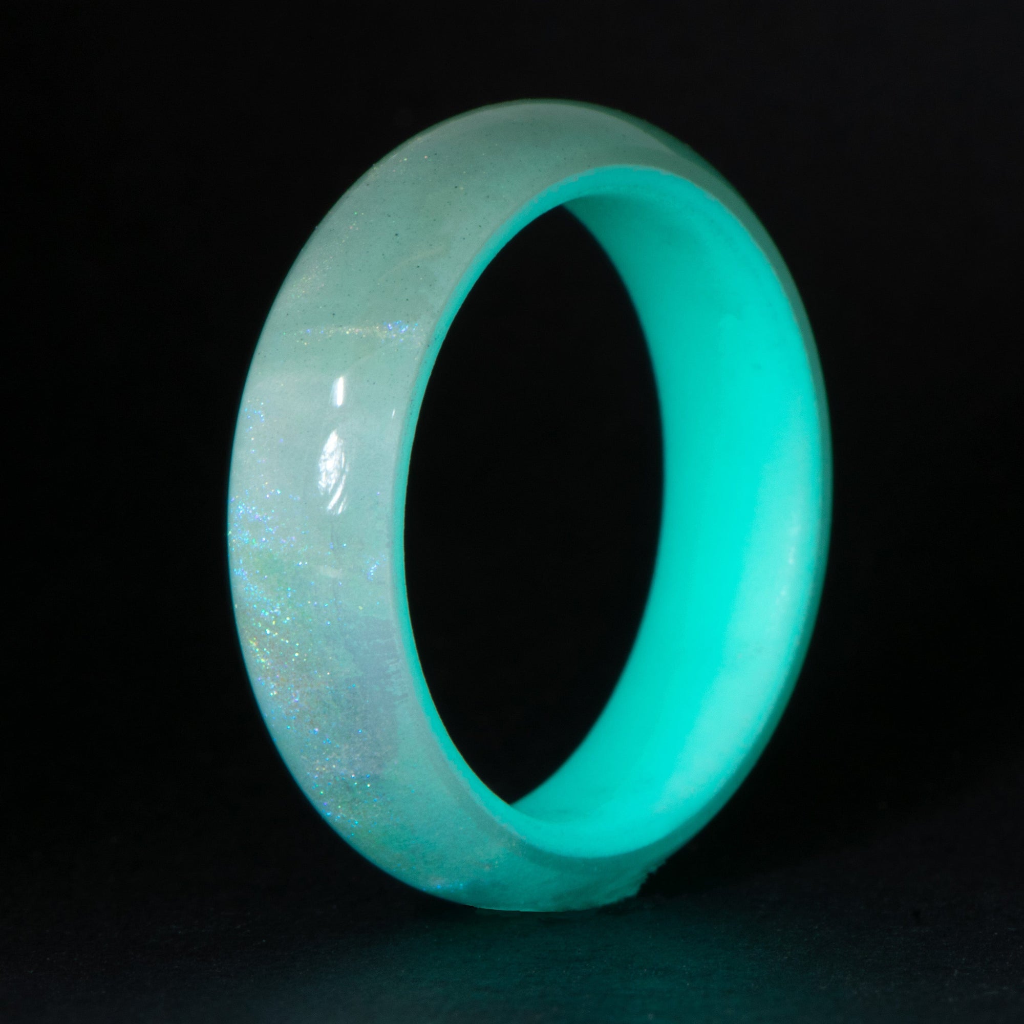 Turquoise glow ring with iridescent polymer exterior on a black background.  