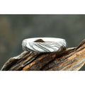 Damascus Steel radius ring with woodgrain pattern on exterior, and smooth silver interior displayed on driftwood.